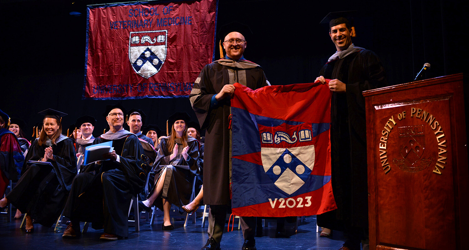 Photo of graduate and alum holding class flag