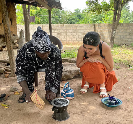 Sulay Camara (left) stokes the coals to prepare to make Attaya as Abby Seeley (right) looks on. (Image: Courtesy of Brianna Parsons)