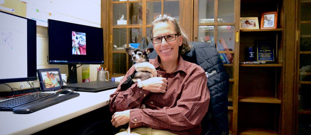 A woman holding dog in an office.