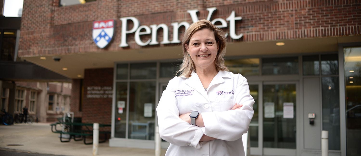A woman in a white coat standing outside the Penn Vet sign.