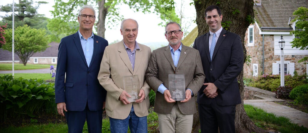 Four people standing in suits with awards.
