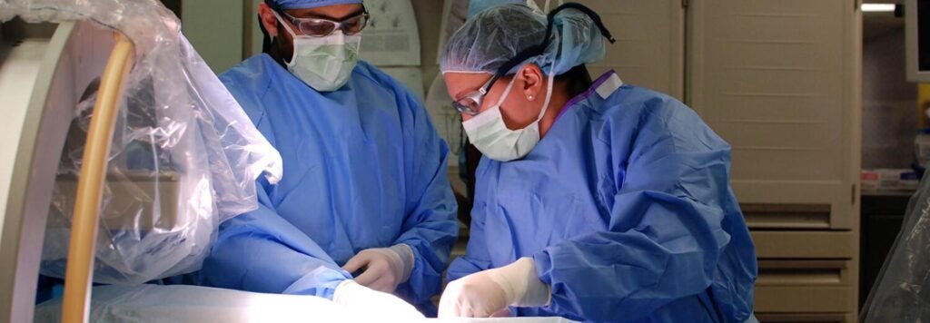 People in blue scrubs and protective eyewear operating.