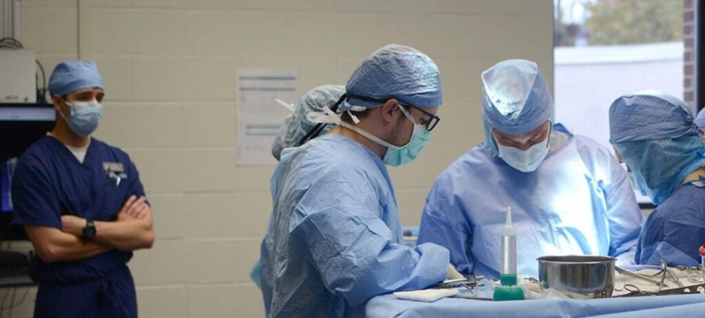 People performing a surgical procedure while in blue scrubs.