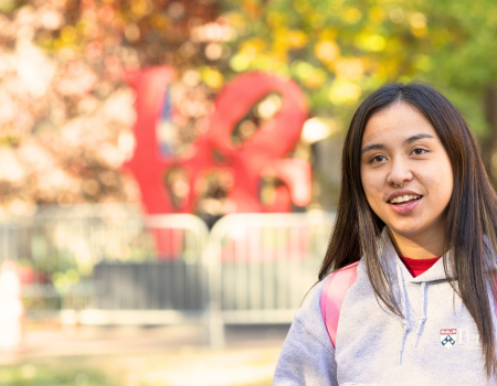 A person smiles while holding a cup of coffee in front of Love Statue