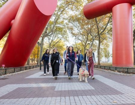 a group of people walking their dog in front of the Covenant sculpture on Penn Campus