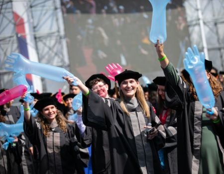 a group of people in graduation gowns with their hands up in the air