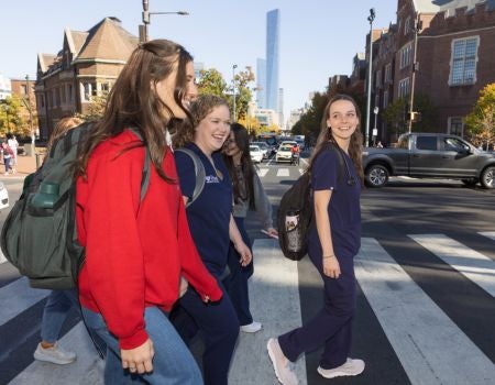 a group of students cross the street in front of a building on campus