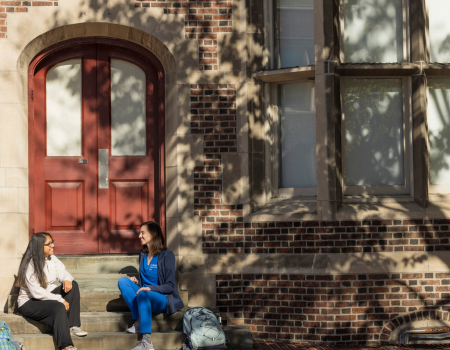 Two students sitting on steps in front of a red door.