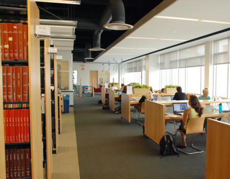 people sitting at desks in a library with books on shelves