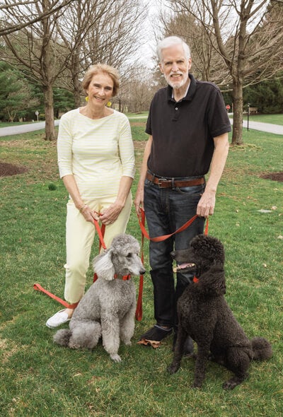 Two people standing in a field with two poodles.