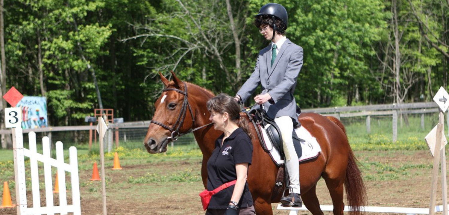 A person sitting on a horse and another person helping