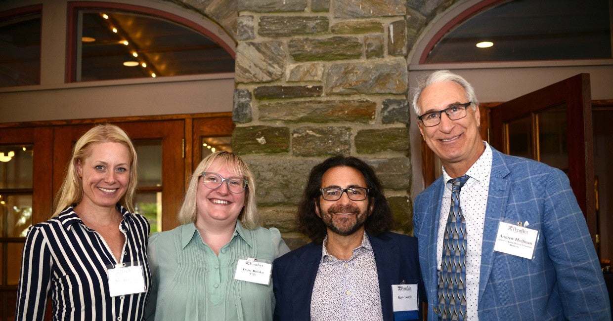 four people standing next to each other in front of a stone wall at an event.