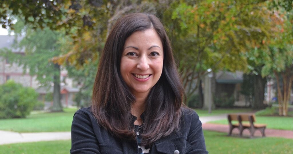 A woman with brown hair standing outside with a bench in the background.