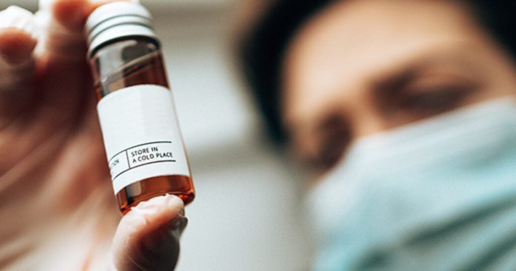 A person in a mask holding a small bottle.