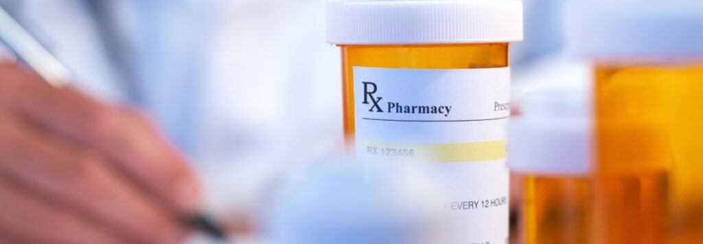 A person filling out a prescription with a bottle in front of them.