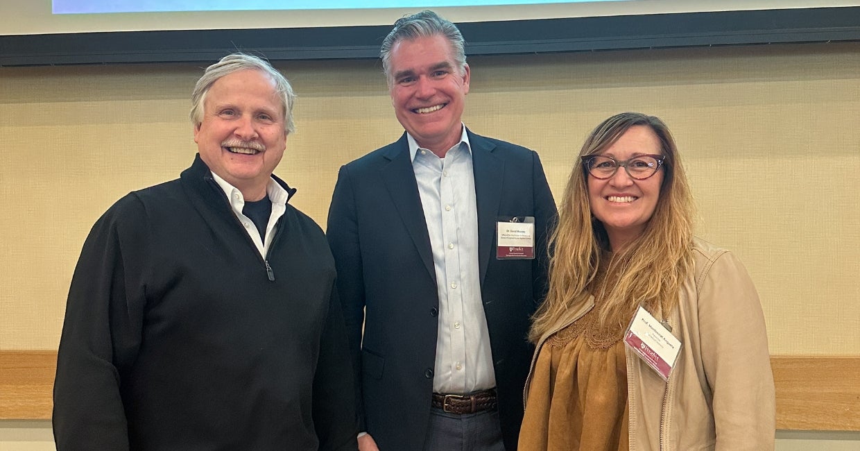 Three people standing together in front of a projector.