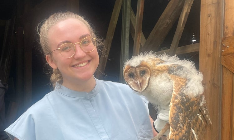 a person in scrubs holding an owl in front of a barn