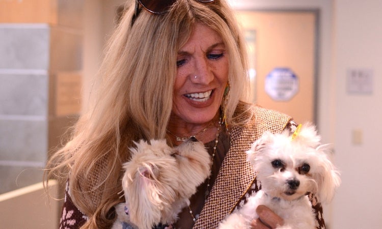 A woman with blonde hair holding two small dogs with white fur.