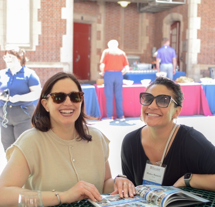 two people sitting at an outdoor table with a magazine