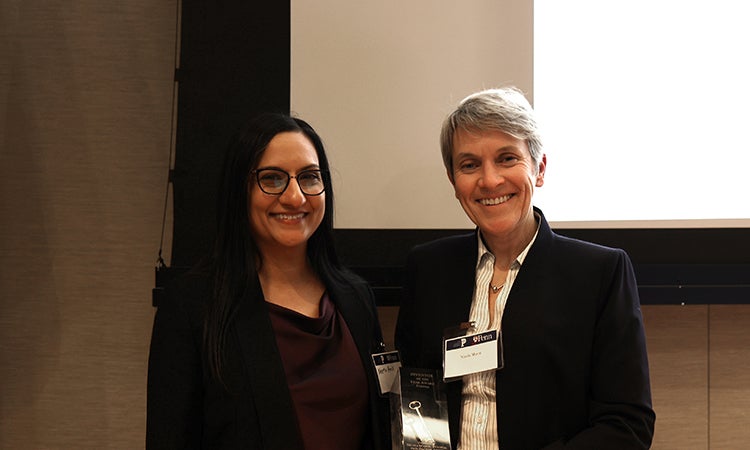 Two people standing with an award in front of a screen.