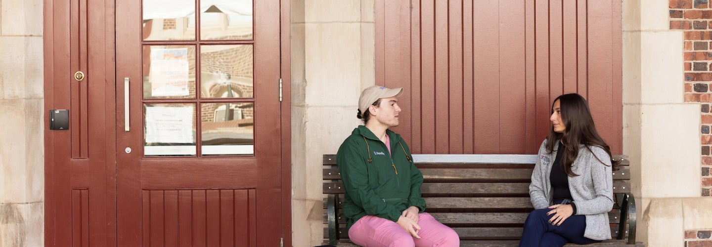 Two people talking outside on a bench.