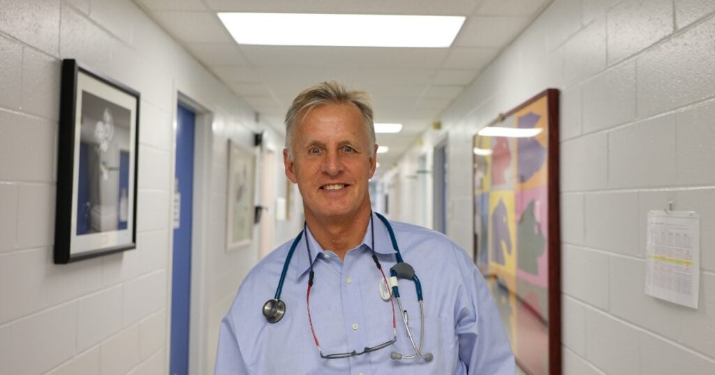 A person in a light blue buttom up shirt stands in a hallway.